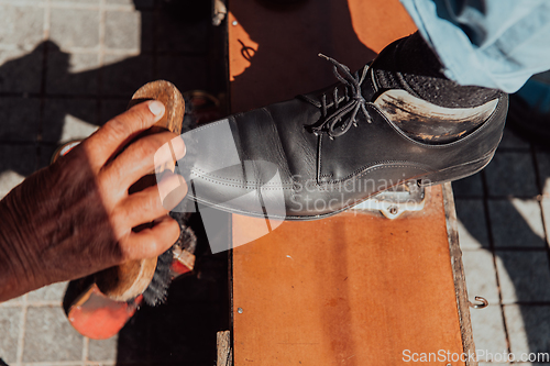 Image of An old man hand polishing and painting a black shoe at street