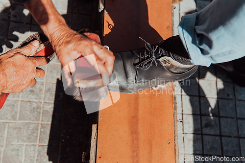 Image of An old man hand polishing and painting a black shoe at street