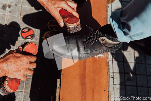 Image of An old man hand polishing and painting a black shoe at street