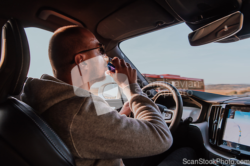 Image of A tired man drinking acoffee while driving a car at sunset. Tired travel and long drive