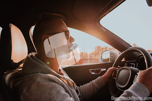 Image of A man with a sunglasses driving a car at sunset. The concept of car travel