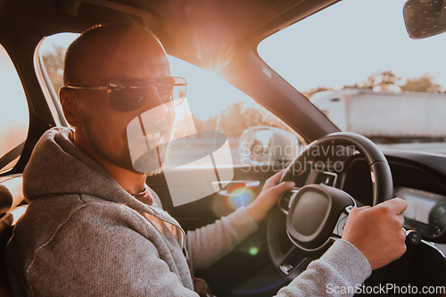 Image of A man with a sunglasses driving a car at sunset. The concept of car travel