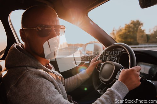 Image of A man with a sunglasses driving a car at sunset. The concept of car travel