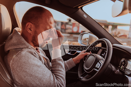 Image of A tired driver holding his head. Exhausted and tired driver driving a car at sunset