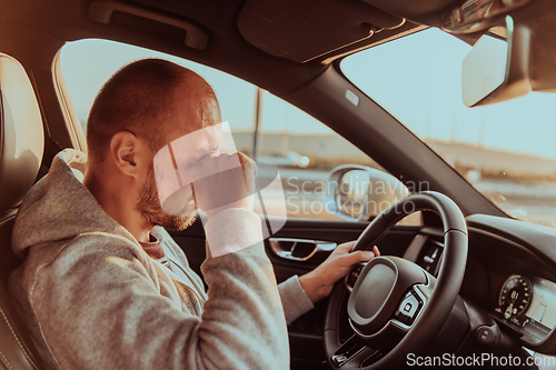 Image of A tired driver holding his head. Exhausted and tired driver driving a car at sunset