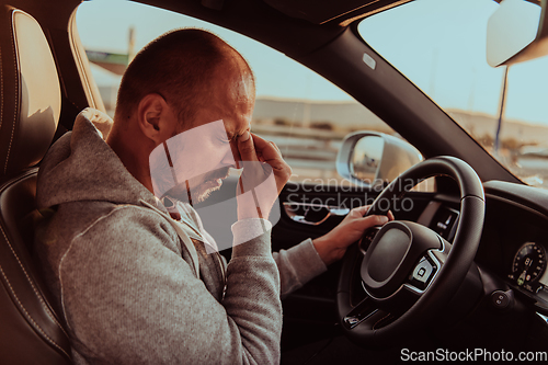 Image of A tired driver holding his head. Exhausted and tired driver driving a car at sunset