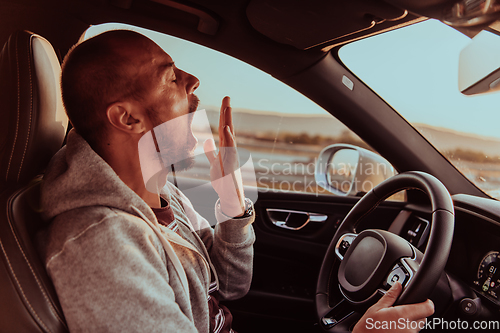 Image of A tired driver yawns while driving a car at sunset