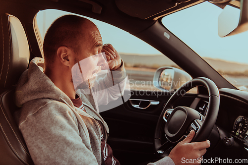 Image of A tired driver holding his head. Exhausted and tired driver driving a car at sunset