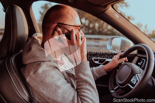 Image of A man with a sunglasses driving a car and talking on smartphone at sunset. The concept of car travel