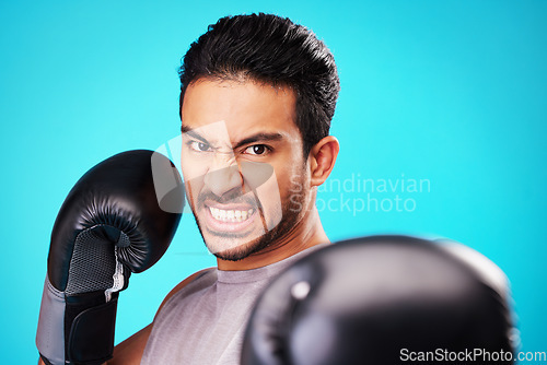 Image of Angry boxer man, studio portrait and punch for workout, training and fitness by blue background. Athlete, boxing gloves and power for exercise, fight and development for performance in combat sports