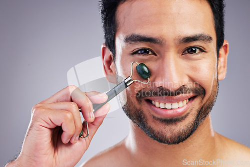 Image of Happy man, portrait or face massage with roller or product for healthy skincare on studio background. Cheek, crystal stone treatment or male model with facial dermatology cosmetic for beauty glow