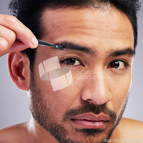 Image of Eyebrow, tweezer and portrait of a man in studio for beauty, hygiene or grooming. Hair removal, epilation and face of serious asian person for skincare, self care or cosmetic tools on grey background