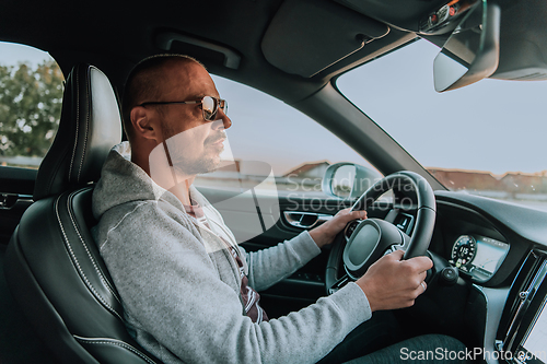 Image of A man with a sunglasses driving a car at sunset. The concept of car travel