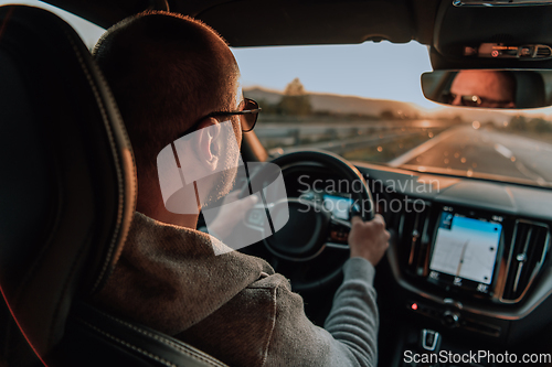 Image of A man with a sunglasses driving a car at sunset. The concept of car travel