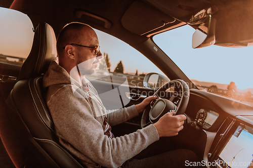 Image of A man with a sunglasses driving a car at sunset. The concept of car travel