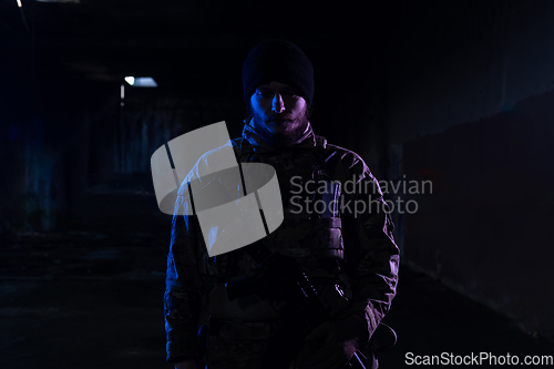 Image of Army soldier in Combat Uniforms with an assault rifle and combat helmet night mission dark background. Blue and purple gel light effect.