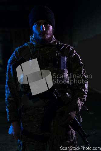 Image of Army soldier in Combat Uniforms with an assault rifle and combat helmet night mission dark background. Blue and purple gel light effect.