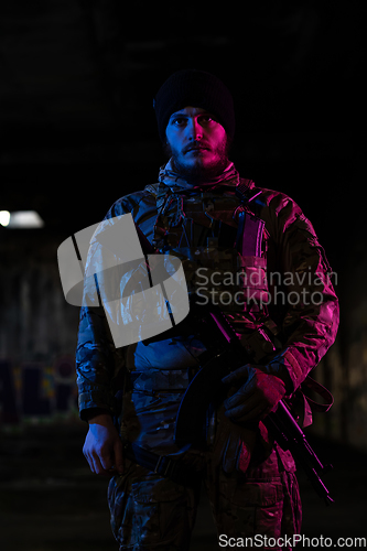 Image of Army soldier in Combat Uniforms with an assault rifle and combat helmet night mission dark background. Blue and purple gel light effect.