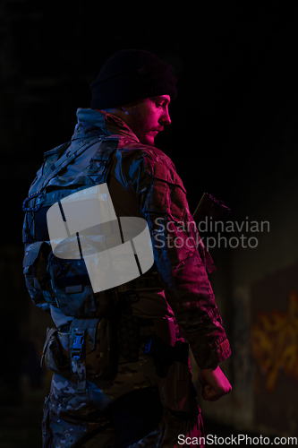 Image of Army soldier in Combat Uniforms with an assault rifle and combat helmet night mission dark background. Blue and purple gel light effect.