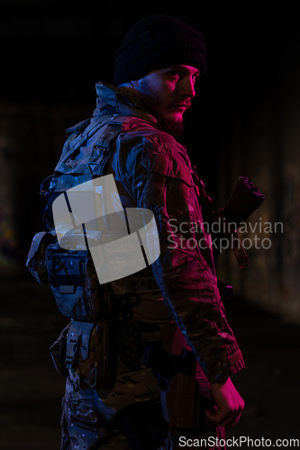 Image of Army soldier in Combat Uniforms with an assault rifle and combat helmet night mission dark background. Blue and purple gel light effect.