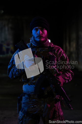 Image of Army soldier in Combat Uniforms with an assault rifle and combat helmet night mission dark background. Blue and purple gel light effect.