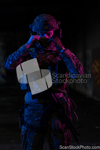 Image of Army soldier in Combat Uniforms with an assault rifle and combat helmet night mission dark background. Blue and purple gel light effect.