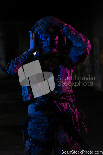 Image of Army soldier in Combat Uniforms with an assault rifle and combat helmet night mission dark background. Blue and purple gel light effect.