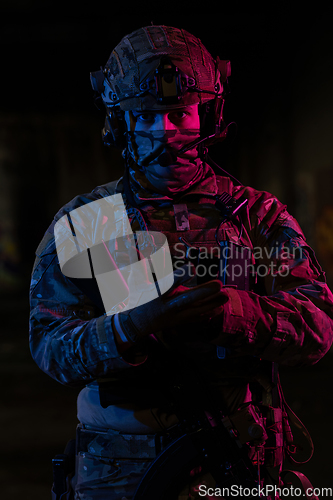 Image of Photo of a fully equipped soldier in black armor tactical vest and gloves standing on black background closeup front view.