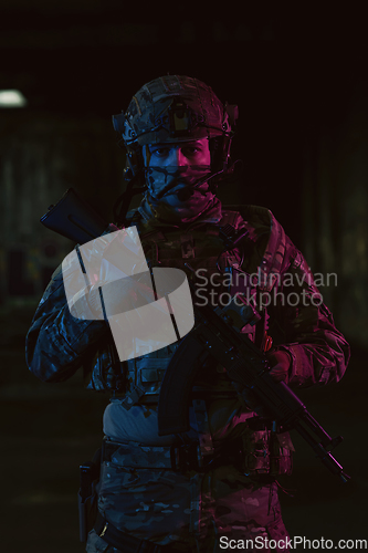 Image of Army soldier in Combat Uniforms with an assault rifle and combat helmet night mission dark background. Blue and purple gel light effect.