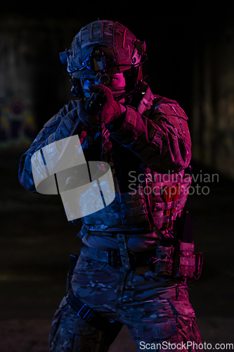 Image of Army soldier in Combat Uniforms with an assault rifle and combat helmet night mission dark background. Blue and purple gel light effect.