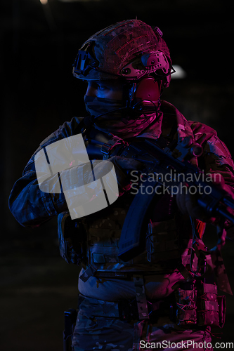 Image of Army soldier in Combat Uniforms with an assault rifle and combat helmet night mission dark background. Blue and purple gel light effect.