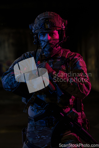 Image of Army soldier in Combat Uniforms with an assault rifle and combat helmet night mission dark background. Blue and purple gel light effect.