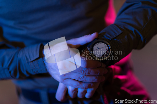 Image of Modern warfare soldier checking navigation, time and other information on a smartwatch. Dark night black background.