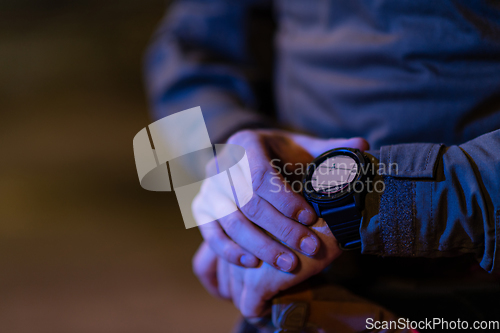 Image of Modern warfare soldier checking navigation, time and other information on a smartwatch. Dark night black background.