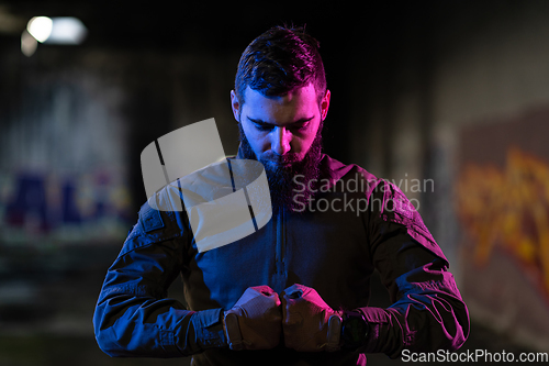 Image of Photo of a fully equipped soldier in black armor tactical vest and gloves standing on black background closeup front view.