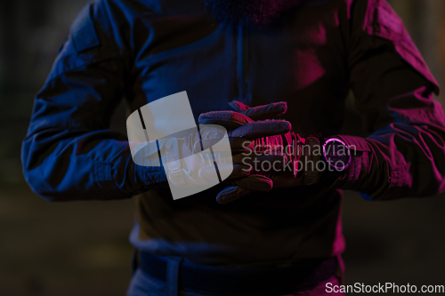 Image of Photo of a fully equipped soldier in black armor tactical vest and gloves standing on black background closeup front view.