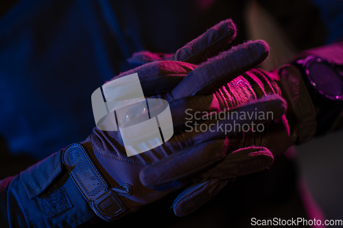 Image of Photo of a fully equipped soldier in black armor tactical vest and gloves standing on black background closeup front view.