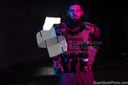 Image of Army soldier in Combat Uniforms with an assault rifle and combat helmet night mission dark background. Blue and purple gel light effect.