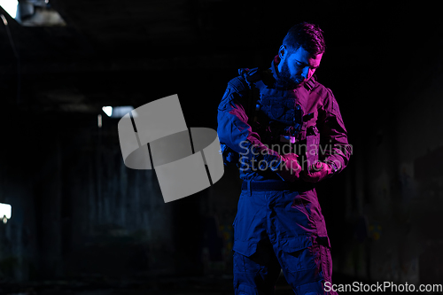 Image of Army soldier in Combat Uniforms with an assault rifle and combat helmet night mission dark background. Blue and purple gel light effect.