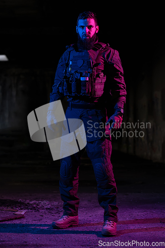 Image of Army soldier in Combat Uniforms with an assault rifle and combat helmet night mission dark background. Blue and purple gel light effect.