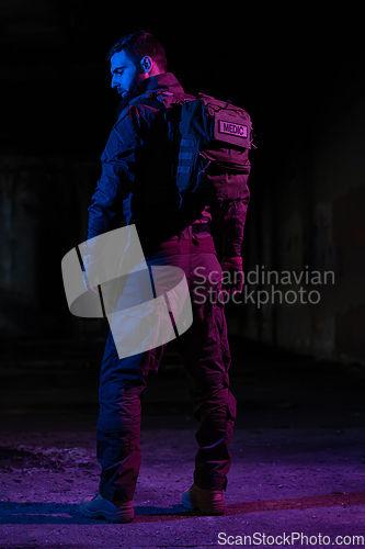 Image of Army soldier in Combat Uniforms with an assault rifle and combat helmet night mission dark background. Blue and purple gel light effect.