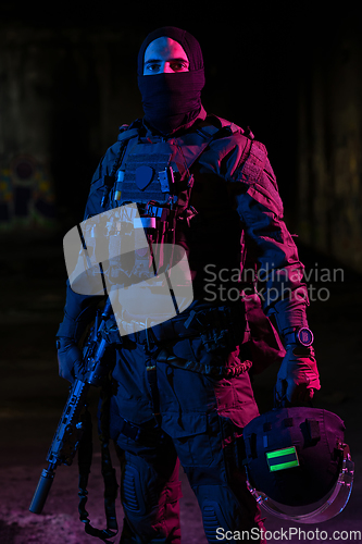 Image of Army soldier in Combat Uniforms with an assault rifle and combat helmet night mission dark background. Blue and purple gel light effect.