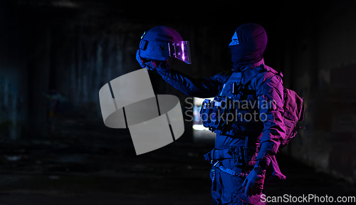 Image of Army soldier in Combat Uniforms with an assault rifle and combat helmet night mission dark background. Blue and purple gel light effect.