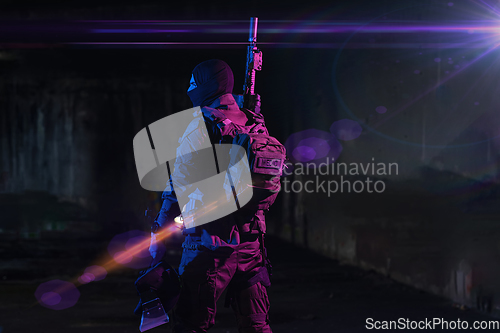 Image of Army soldier in Combat Uniforms with an assault rifle and combat helmet night mission dark background. Blue and purple gel light effect.