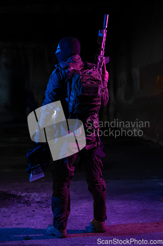 Image of Army soldier in Combat Uniforms with an assault rifle and combat helmet night mission dark background. Blue and purple gel light effect.