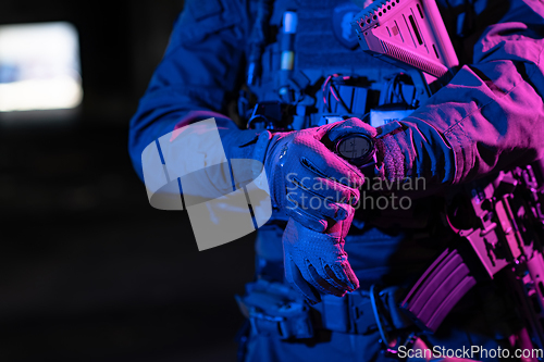 Image of Modern warfare soldier checking navigation, time and other information on a smartwatch. Dark night black background.