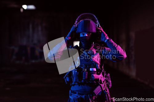 Image of Army soldier in Combat Uniforms with an assault rifle and combat helmet night mission dark background. Blue and purple gel light effect.