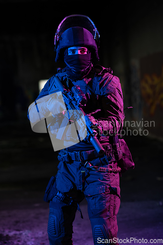 Image of Army soldier in Combat Uniforms with an assault rifle and combat helmet night mission dark background. Blue and purple gel light effect.