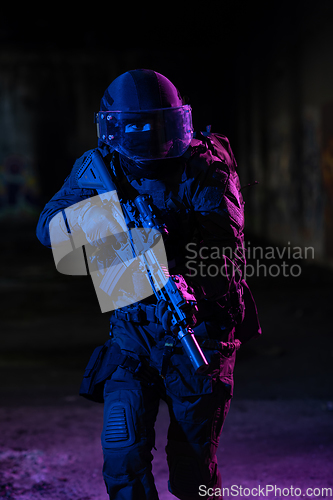 Image of Army soldier in Combat Uniforms with an assault rifle and combat helmet night mission dark background. Blue and purple gel light effect.