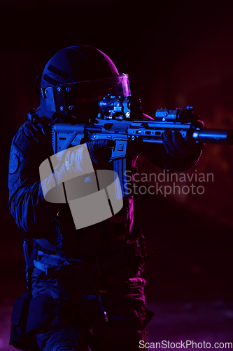 Image of Army soldier in Combat Uniforms with an assault rifle and combat helmet night mission dark background. Blue and purple gel light effect.